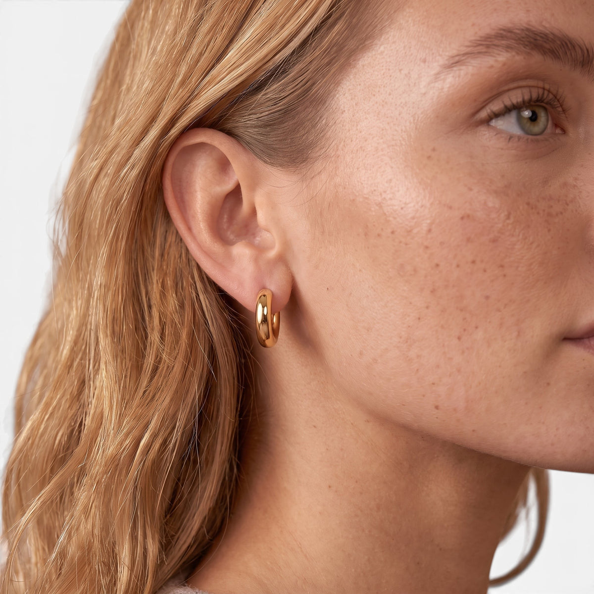 Evervanta dainty gold huggie hoop earrings worn on a woman's ear for a subtle and elegant everyday look.