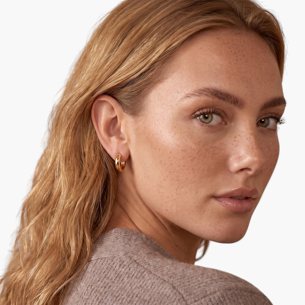 Evervanta dainty gold huggie hoop earrings worn by a woman with blonde hair looking over her shoulder