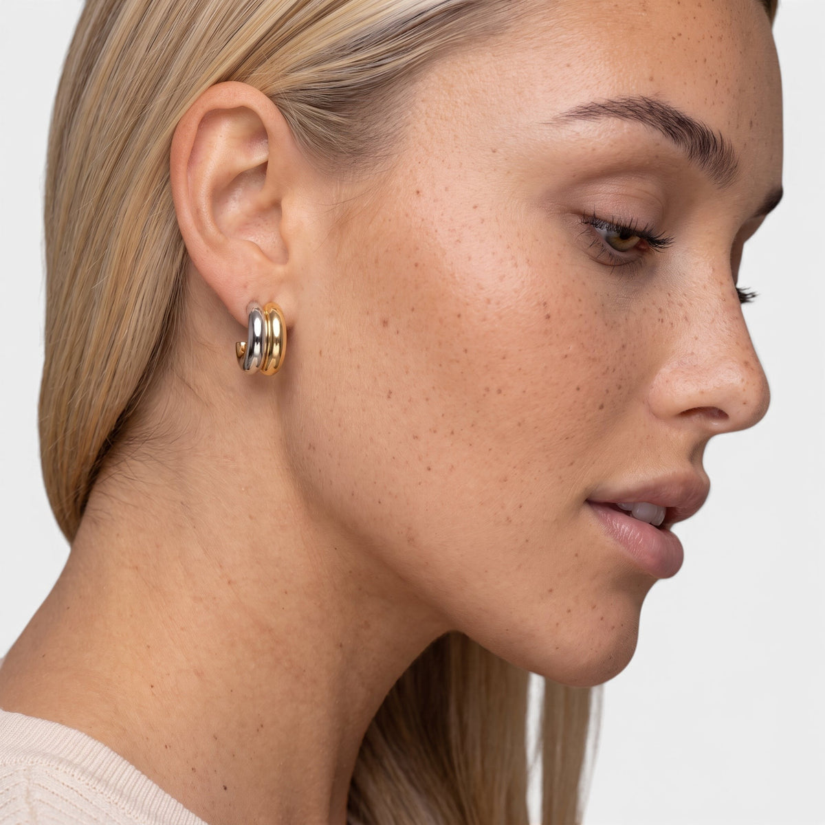 Evervanta two-tone huggie hoop earrings featuring 18K gold and silver plating worn on a woman's ear